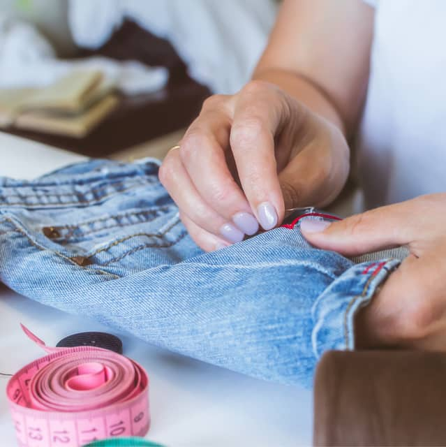 A person skillfully sewing a pair of blue jeans, focused on the intricate details of the fabric and stitching.