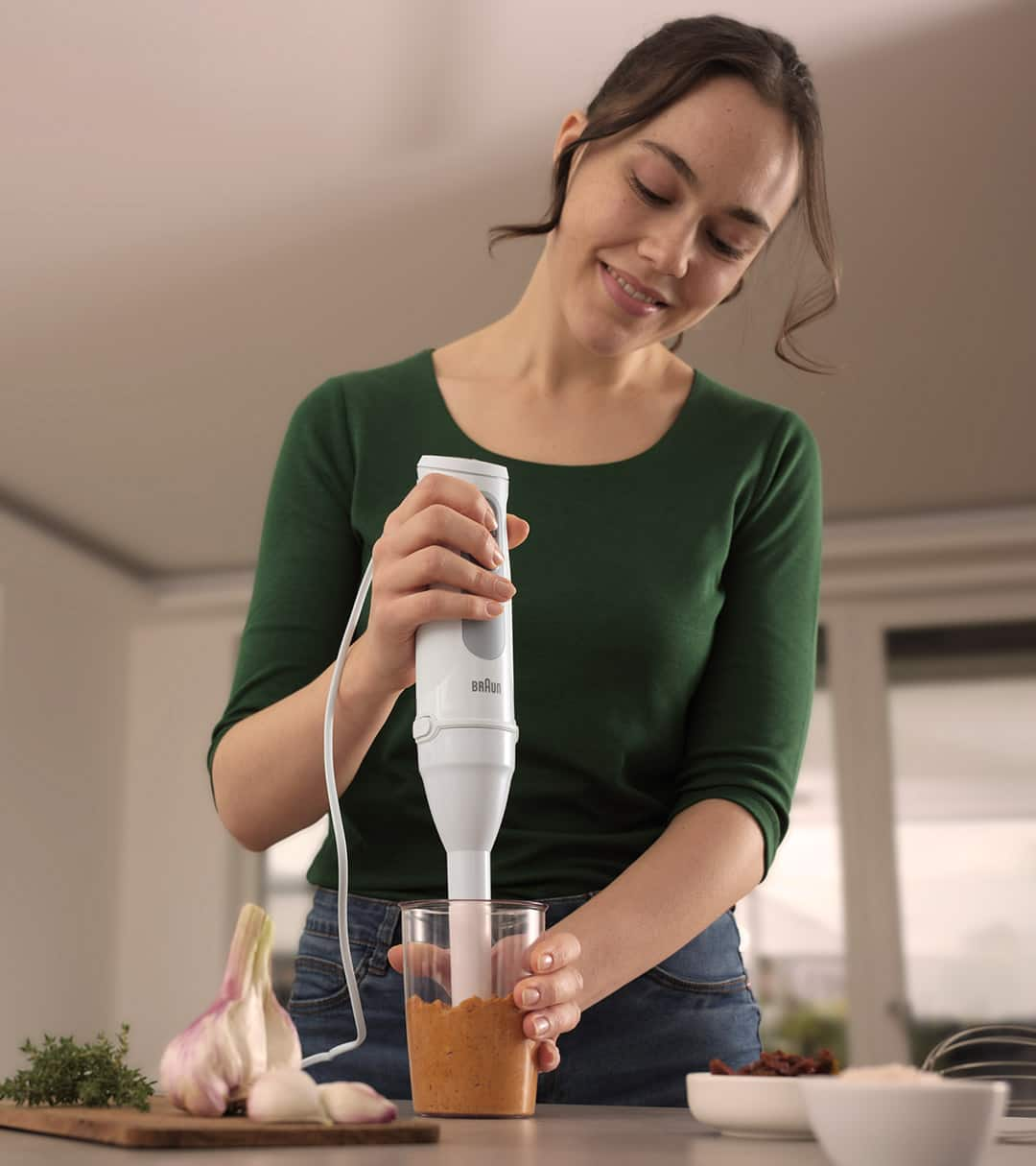 Woman at the kitchen counter preparing a vegetable mash with the Braun MultiQuick 5 with Small Portion Shaft accessory.