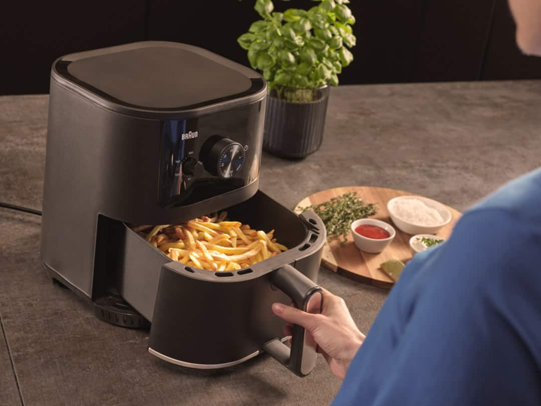 Female hand opening the drawer of Braun's MultiFry 3 airfryer, revealing crunchy french fries