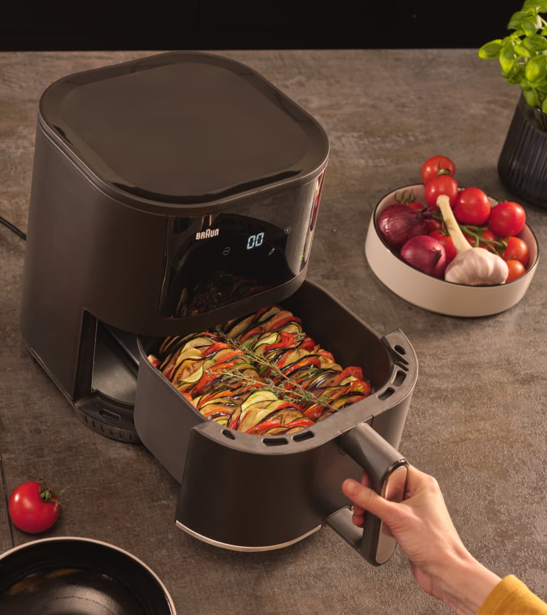 Female hand opening the drawer of Braun's MultiFry 3 airfryer, revealing fried vegetables