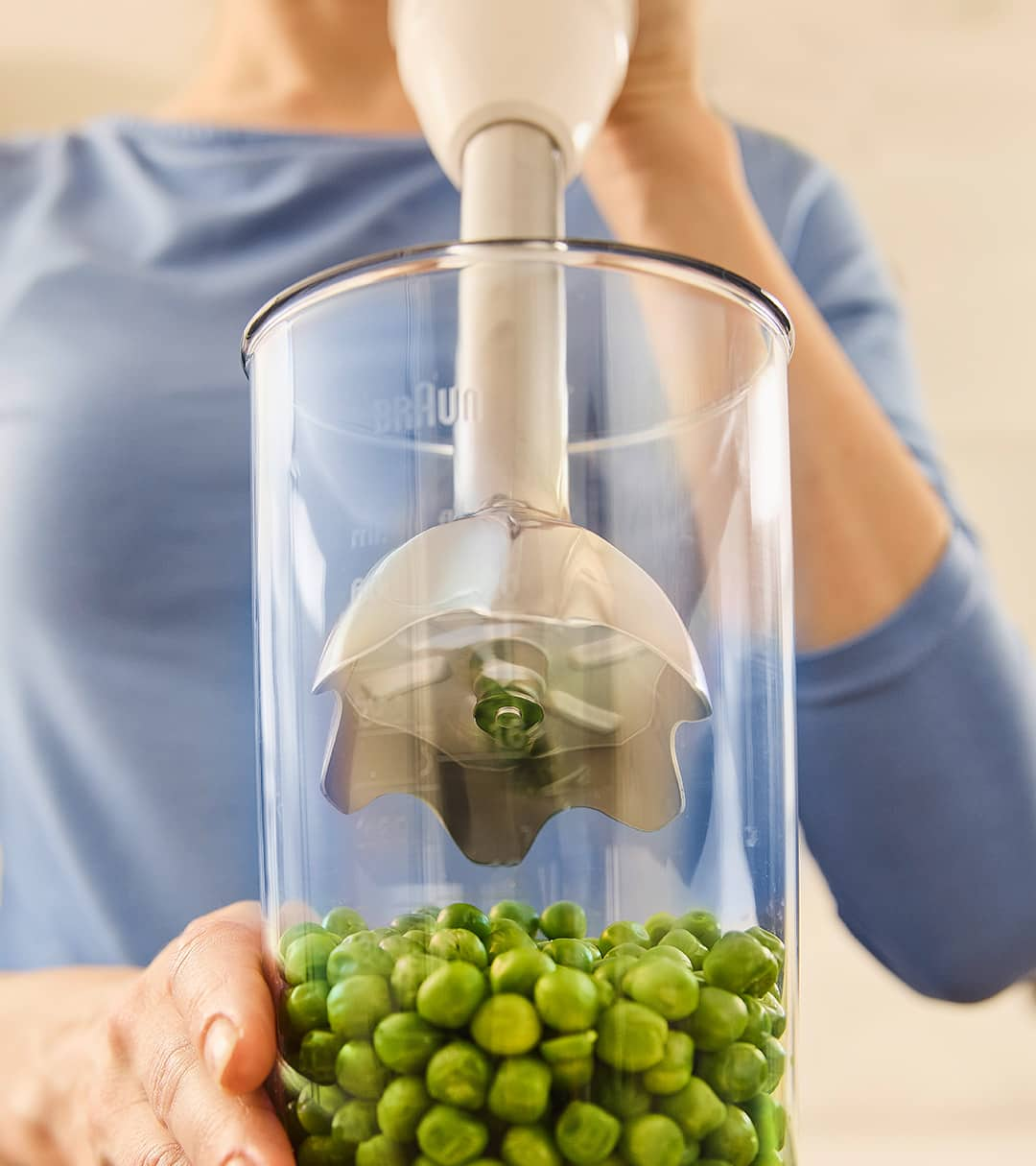 A woman displays a jar of peas, emphasizing the freshness and vibrant color of the vegetables inside.