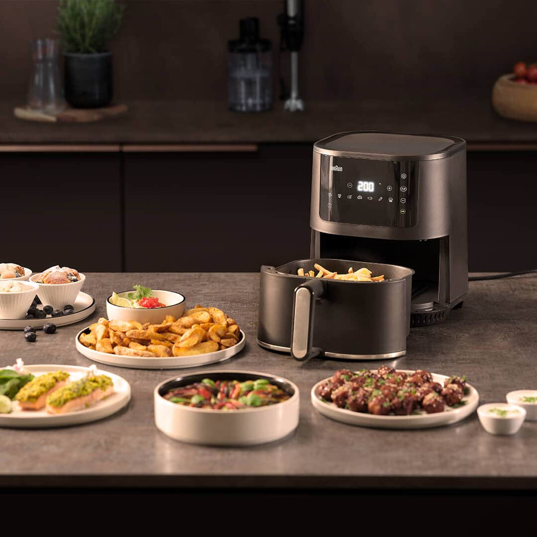 Braun's  MultiFry 3 Air fryer on a kitchen deskt surroundede by delicios Food on plates such as Baked potatos, meat balls e.g.