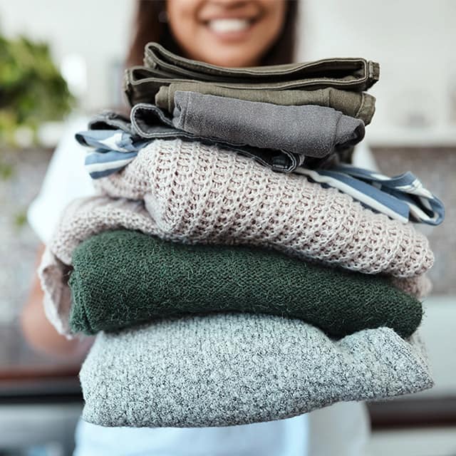 Young woman holding a plie of folded laundry.