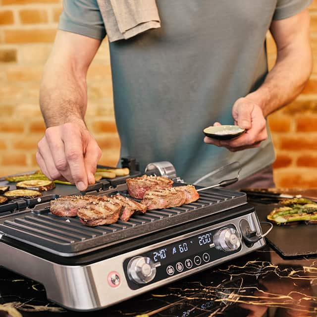 Man seasoning steak grilled on Braun MultiGrill 9 Pro multifunctional contact grill.