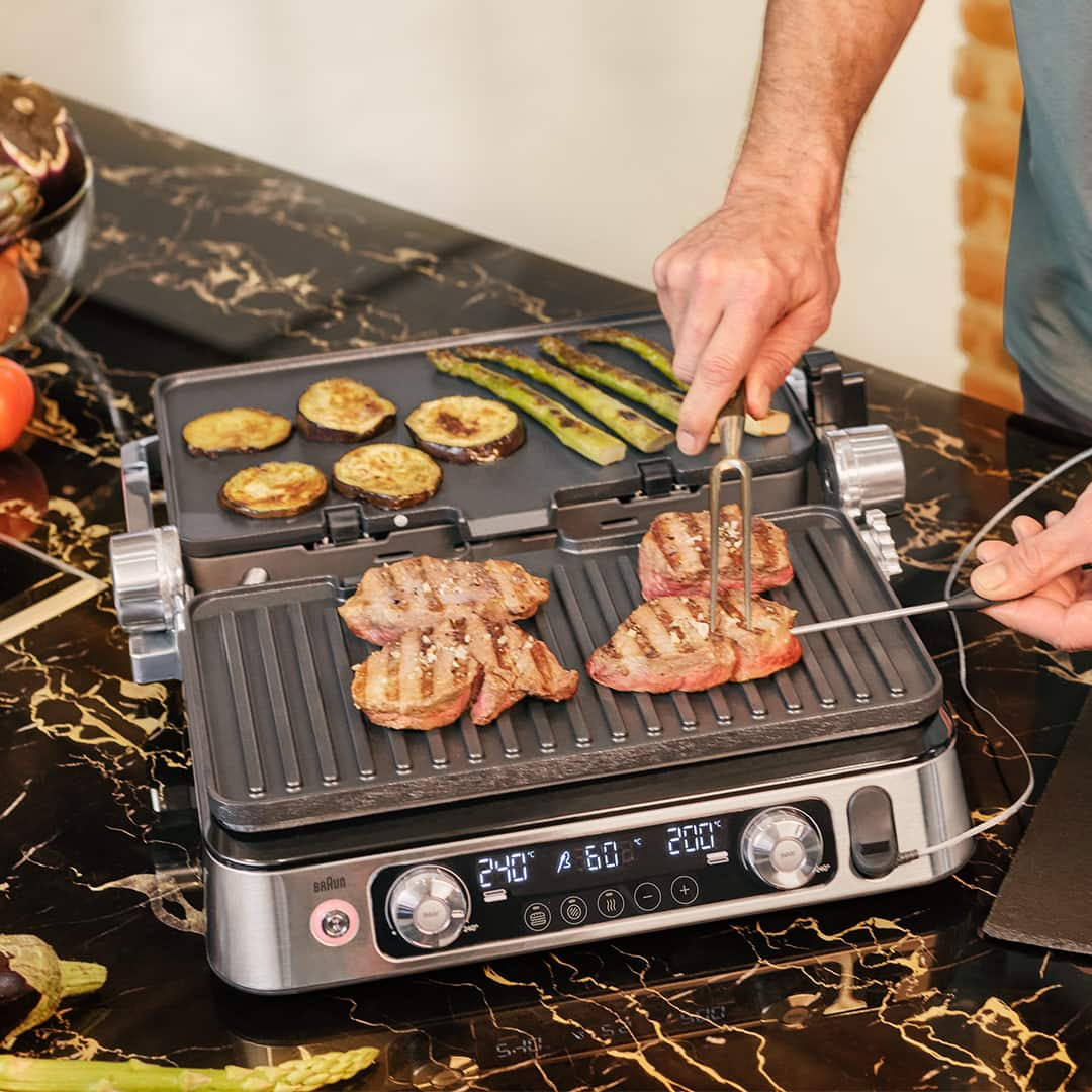 A man grilling steak alongside colorful vegetable